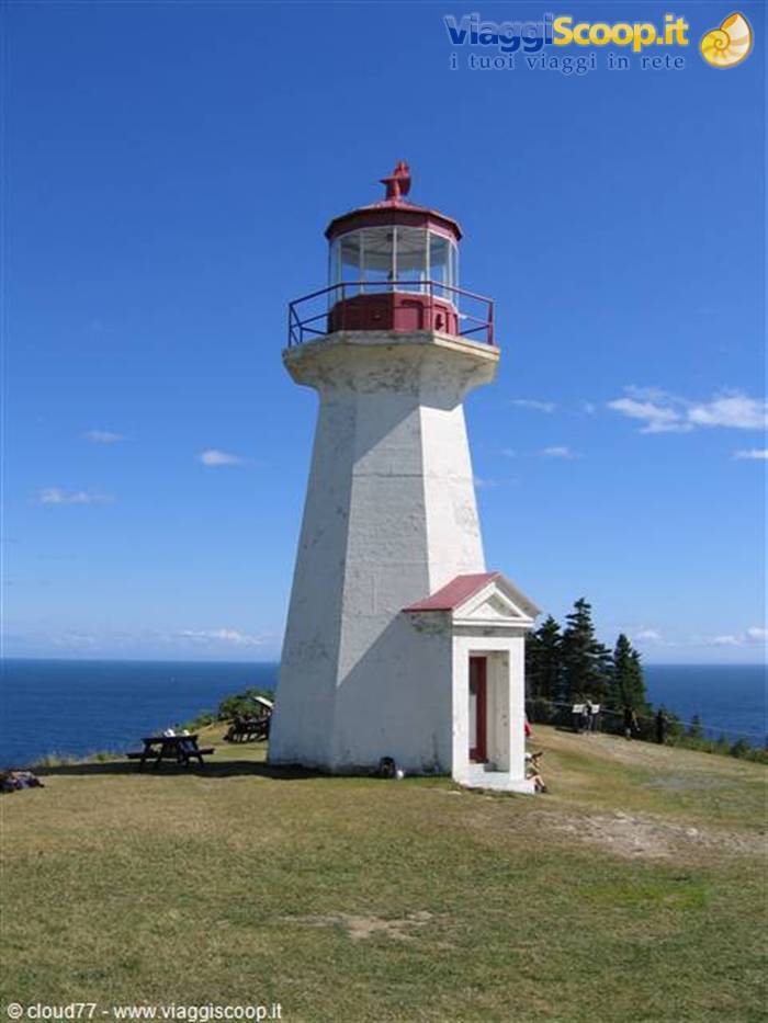 White lighthouse with red lantern on grassy cliff, Cape Enrage