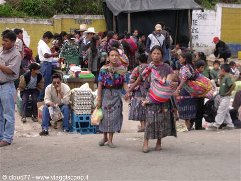 Maya women carrying babies in slings walk through Chichicastenango market stalls