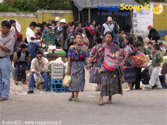 Maya women carrying babies in slings walk through Chichicastenango market stalls