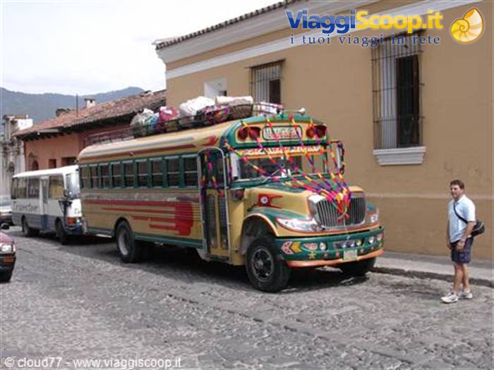 Colorful chicken bus loaded with luggage on cobblestone street, tourist nearby