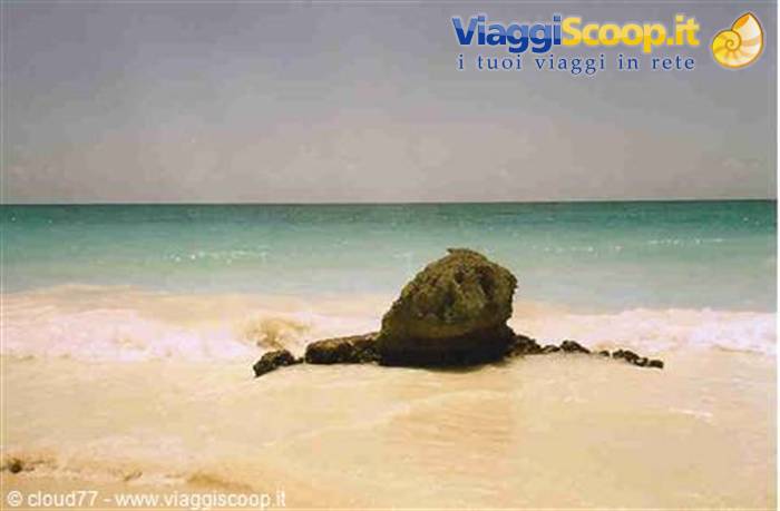 Dark rock on white sand beach, turquoise waves washing over it