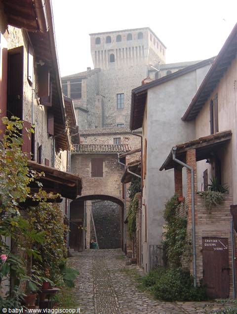 Cobbled alley between stone houses, castle with Ghibelline merlons above