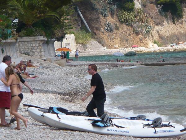 Man in black drags a white kayak onto the pebble beach