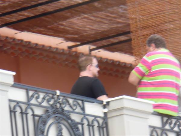 Two men on a terrace with wrought iron railing under a cane roof