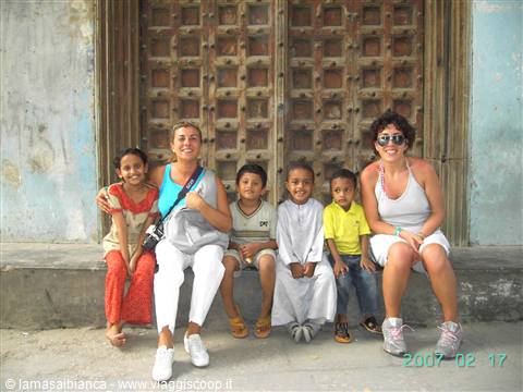 Two smiling women with four children sitting in front of a large wooden door