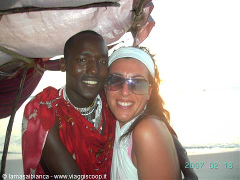 Tourist smiling with Maasai man in red shuka and beaded necklaces on beach