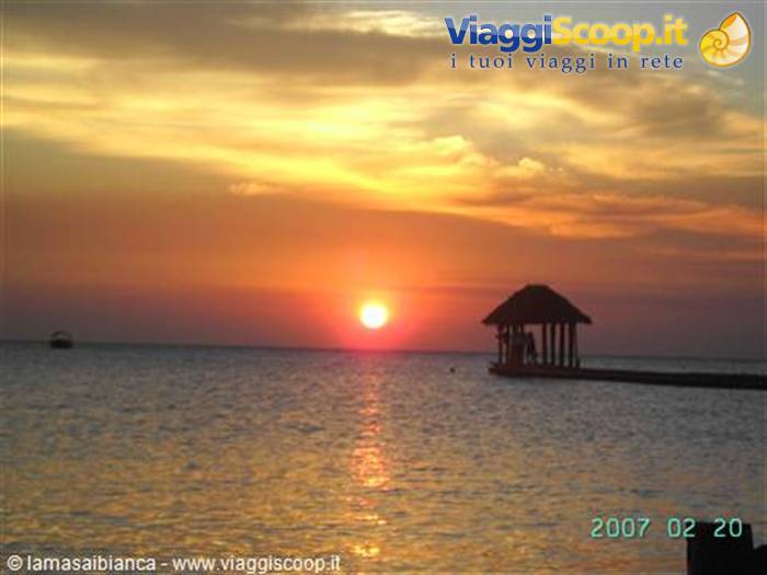 Low sun over the ocean, wooden pier with thatched hut backlit