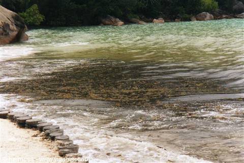 Turquoise water over sand, granite boulders and a wooden boardwalk