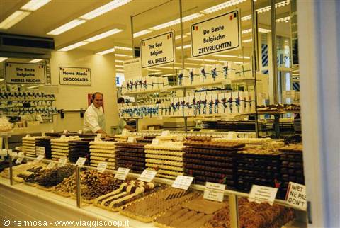 Vendor behind glass counter full of Belgian chocolates and sweets