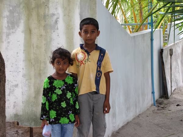 Boy and girl standing beside a white wall under palm trees