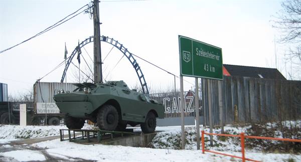 Military armored vehicle displayed on rails beside green road sign to Székesfehérvár, snow on ground