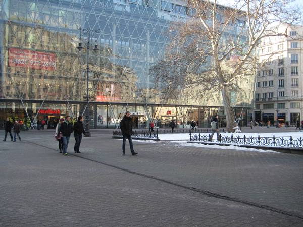 People walk on snowy cobblestones in front of a glass department store facade