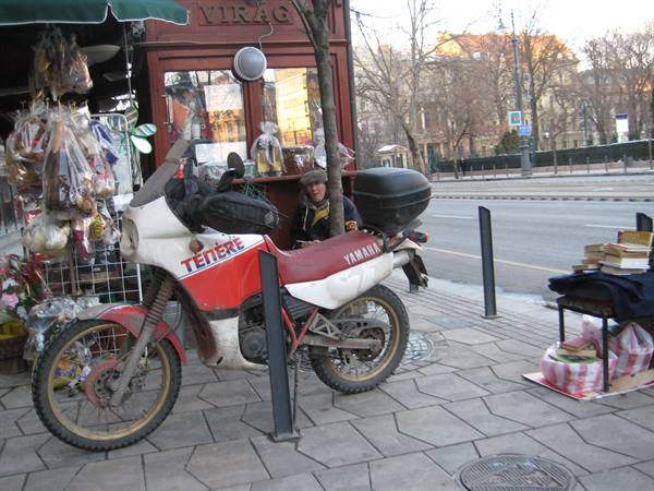 Red and white Yamaha Ténéré motorcycle parked by a street kiosk