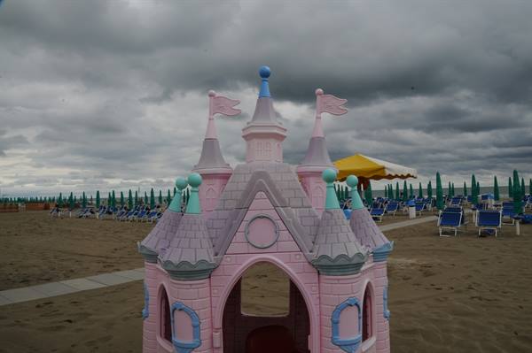 Pink plastic children's castle on the beach, closed umbrellas and cloudy sky
