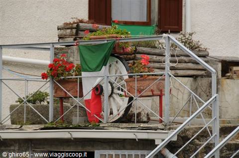 Italian flag and wooden wheel decorating a balcony with red flowers