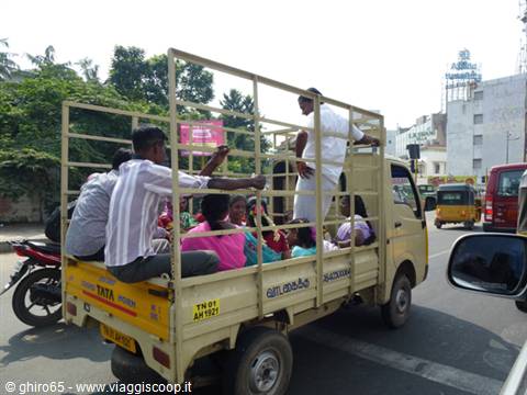 Yellow Tata truck loaded with passengers driving through an Indian street