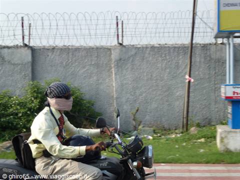 Motorcyclist with covered face and headwrap riding past a concrete wall