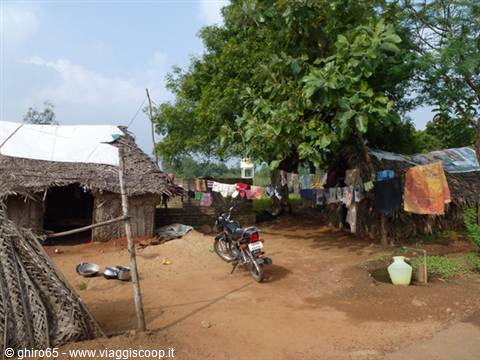Motorbike parked among mud and thatch huts, laundry drying under a large tree