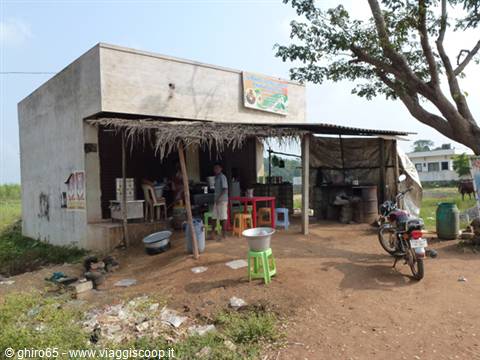 Small concrete stall with thatched awning, colorful plastic stools and parked motorbike