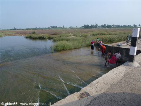 Women washing colorful clothes in a water canal among green fields