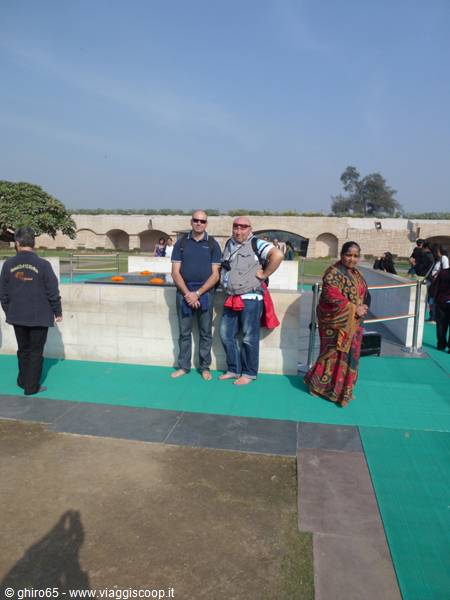 Barefoot tourists at Raj Ghat, black marble memorial with orange flowers