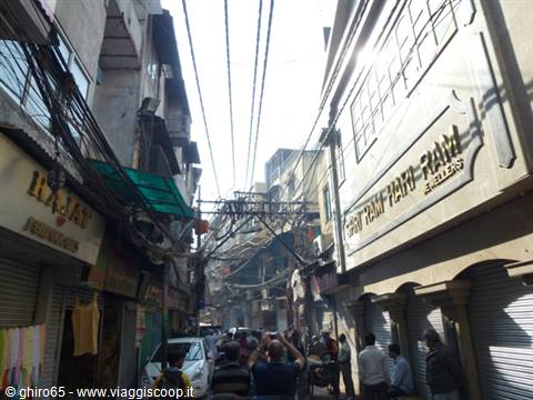Crowded alley between shops with green awnings and tangled overhead electric cables