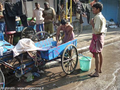 Man washing a blue cart on the street while another man watches