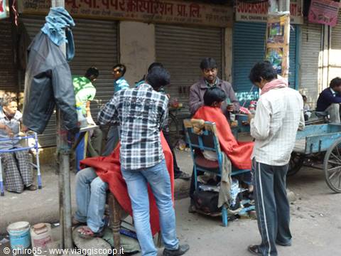 Street barbers cutting hair, seated clients draped in red capes by closed shops