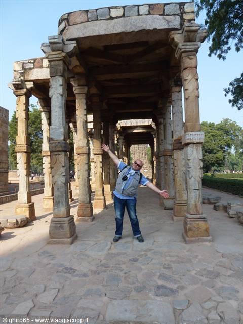 Tourist arms outstretched beneath carved stone columns at the Qutb complex