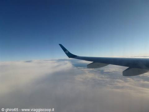 Airplane wing above thick white clouds, clear blue sky