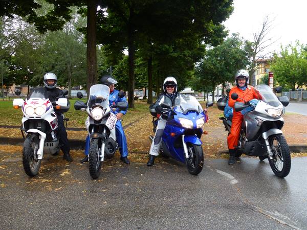Four helmeted riders on touring motorcycles, wet asphalt, green trees