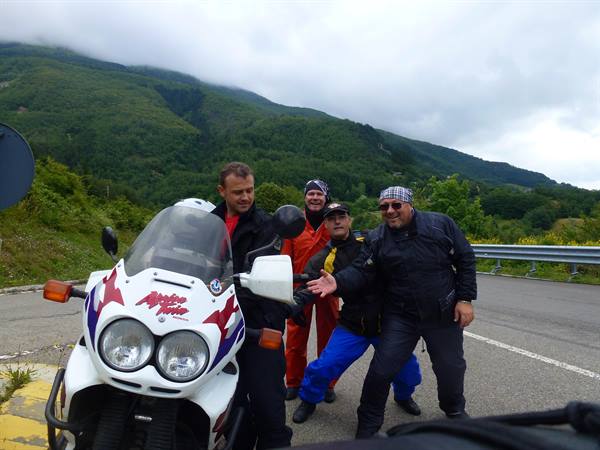 Four motorcyclists posing beside a white BMW bike on a mountain road