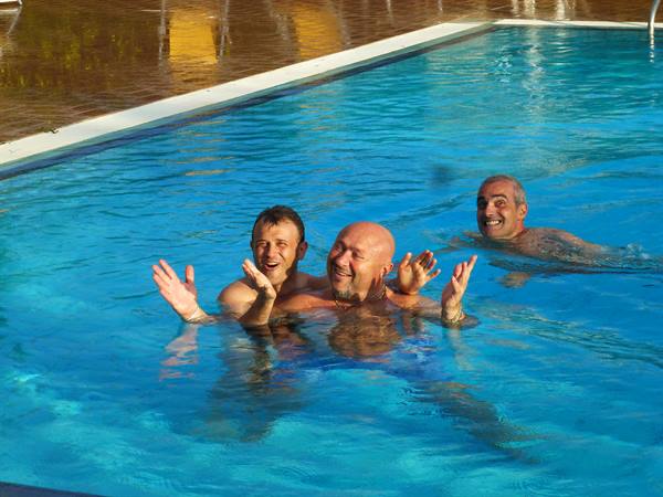 Three smiling men playing in the blue water of a swimming pool