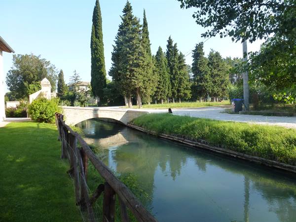 Stone bridge over green canal surrounded by cypress trees and lawn