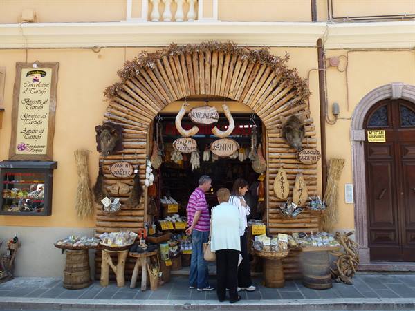 Shoppers at a wood-fronted food shop with hanging cured meats