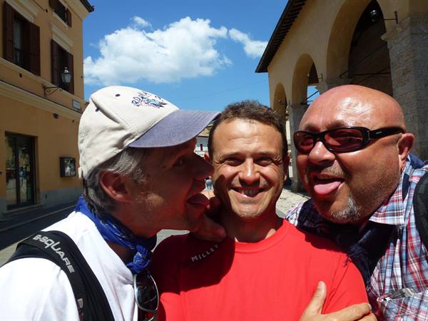 Three friends joking under medieval stone arcades in a sunny village