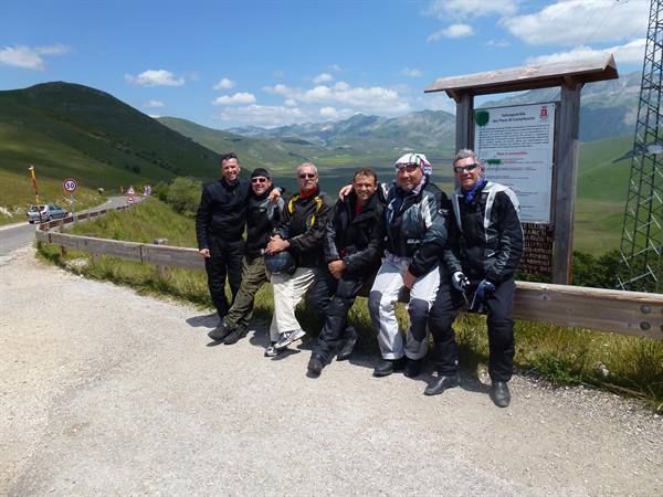 Six motorcyclists posing next to a wooden sign in the Sibillini mountains