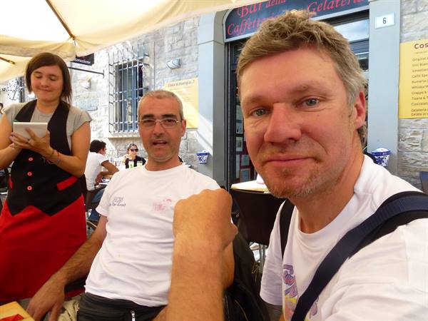 Selfie of two men in white t-shirts outside a gelato café under awnings