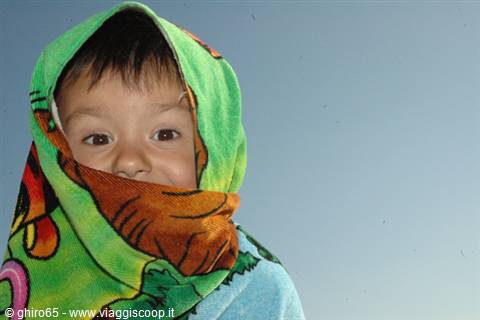 Child with face wrapped in a colorful towel against the sky