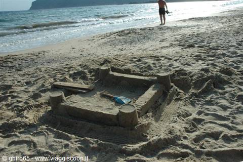 Square sandcastle with towers on the beach, child by the shoreline