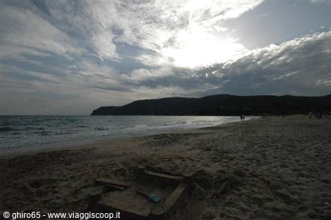 Sandy beach with waves at dusk, dark hills and cloudy sky