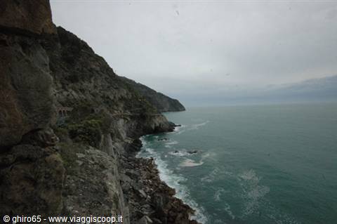 Rocky cliffs plunging into green sea, grey sky, waves on the rocks