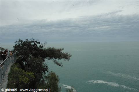 Tourists on a railed terrace above the green sea under cloudy sky