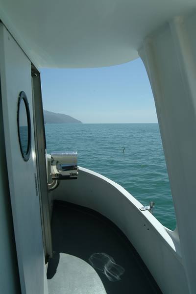 Inside a white boat with porthole, blue sea and mountainous coastline in distance