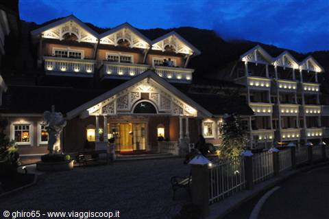 Illuminated wooden grand hotel at night, entrance with statues and mountain behind