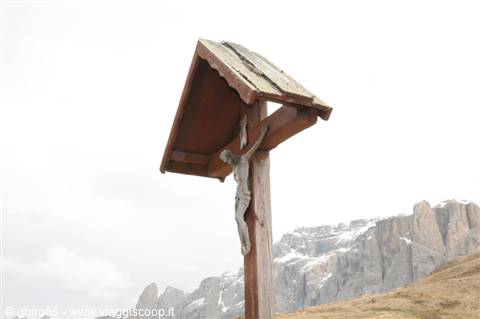 Wooden wayside cross with Christ statue under a roof, snowy Dolomites behind
