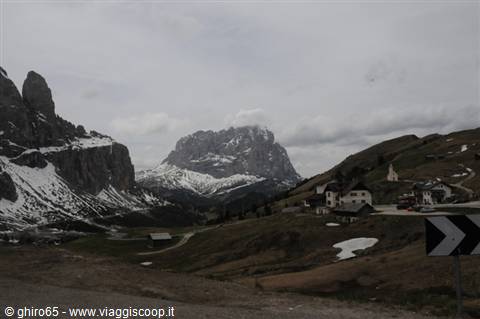Gardena Pass, houses and chapel under snowy Dolomites peaks beneath grey clouds