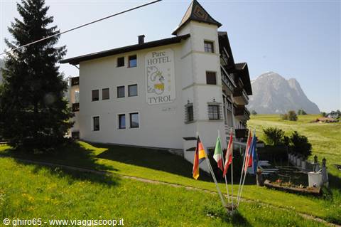 White Hotel Tyrol with turret, colorful flags on green lawn, Dolomite peak behind