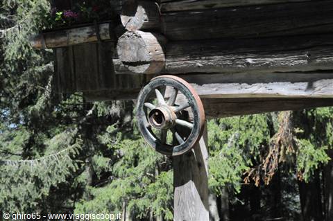 Old wooden cart wheel hanging under the beam of a log cabin