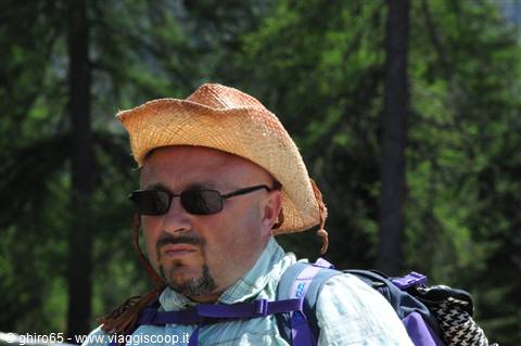 Man wearing straw hat and hiking backpack among firs